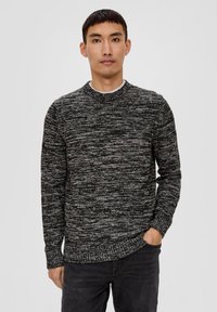 Dzianinowy sweter w odcieniach czerni i szarości, okrągły dekolt, długie rękawy, fakturowana tkanina, z prążkowanym wykończeniem u dołu i na mankietach. Zestawiony z ciemnymi dżinsami.