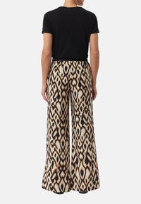 Wijduitlopende broek met een crèmekleurige achtergrond, voorzien van een gedurfde zwart-oranje dierenprint. In combinatie met een zwarte top met korte mouwen.