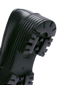 Chaussure en cuir noir avec semelle en caoutchouc épaisse et rainurée, présentant des crampons profonds et angulaires ainsi que la taille 36 indiquée en dessous.