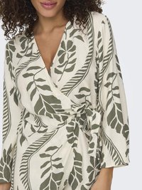 Vestido blanco de manga larga con estampado de hojas verdes, con una cintura ajustada. Hecho de una tela suave con una textura lisa.