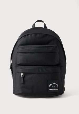 Sort nylon rygsæk med en rund form, der har en frontlomme med lynlås, diskret mærkning og et håndtag til at bære i toppen. Glat tekstur.