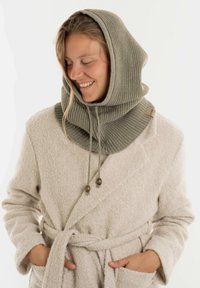 Lichtgrijze ribgebreide hoodie met een brede kol, verstelbare trekkoorden en houten kraalaccenten, gedragen over een crèmekleurige ochtendjas.