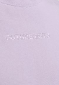 Camiseta de algodón de color púrpura claro con cuello redondo y texto bordado "FUTURE EDTN" en un color ligeramente contrastante en la parte frontal.