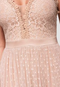 Robe en dentelle beige avec motifs floraux sur le corsage, décolleté plongeant en V et jupe en tulle transparent à pois avec ceinture en satin.