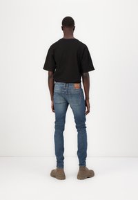 Svart kortermet skjorte brukt med lyseblå denimjeans. Jeansen har et merke bak og er komplementert med beige støvler.