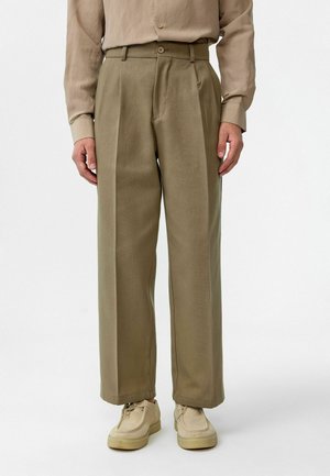 Khaki wijde broek met een hoge taille, plooien en een gestructureerde stof. Gecombineerd met beige schoeisel voor een gecoördineerde look.