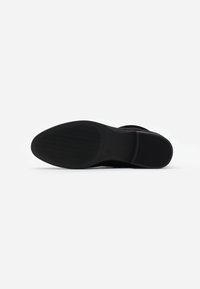 Suela de zapato negra con una sección superior lisa y un agarre de goma texturizada. Presenta una punta redondeada y un sutil patrón de ondas en la parte inferior.