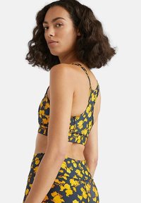 Sujetador deportivo floral en azul marino con flores amarillas, que presenta tirantes finos, un diseño ajustado y una tela texturizada para ropa deportiva.