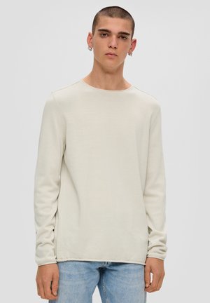 Lichtbeige lange mouwen shirt van een zacht materiaal met een ronde halslijn en naadloze manchetten, gecombineerd met lichtblauwe denim jeans.