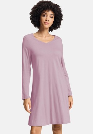 Woman with curly hair wearing a long-sleeve, light purple knee-length dress against a plain background.