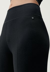 Svarta högmidjade leggings med en texturerad fiskbensmönster, med en liten matt svart logotypdetalj på midjan.