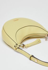 Sac à main en cuir jaune de forme croissant, avec un bord noir, un détail pompon, et une fermeture éclair dorée. Doté d'une bandoulière amovible pour plus de polyvalence.