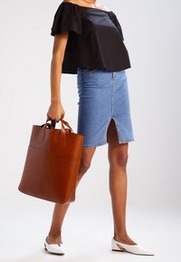 Top nero off-the-shoulder, gonna in denim azzurro chiaro con spacco frontale, ballerine bianche e una grande borsa a tracolla in pelle marrone con doppio manico.