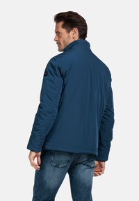 Marineblauwe gewatteerde jas met een hoge kraag en ritssluiting. Bevat een logopatch op de linkerarm en gestikte schouderaccenten.