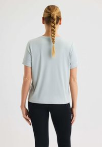 Ljusgrå kortärmad atletisk topp med rund hals, tillverkad av slät tyg. Kombinerad med svarta leggings och en flätad frisyr.