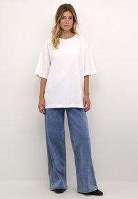 T-shirt bianco oversize con maniche corte, taglio dritto, abbinato a jeans a gamba larga blu chiaro. Design semplice, con dettagli minimi.