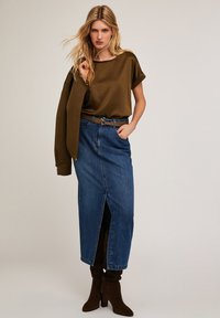 Olivgrön satin-top, blå denimkjol med slits, brunt bälte och bruna mockaskor i knähöjd, med en avslappnad passform och slät textur.