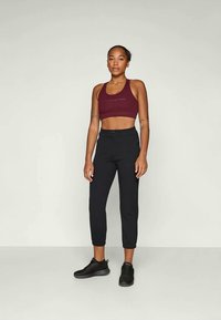 Sujetador deportivo marón y pantalones de chándal negros ajustados, con una textura suave, costuras reforzadas y un logo de marca en el sujetador. Zapatillas negras.