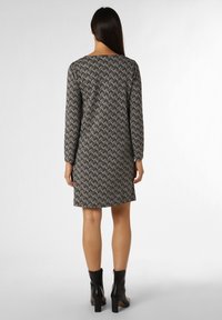 Schwarz-weiß gemustertes Kleid mit langen Ärmeln, gerader Silhouette und Rundhalsausschnitt, kombiniert mit schwarzen Knöchelstiefeln.