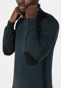 Dunkelblauer gestrickter Pullover mit hohem Kragen, geripptem Muster an den Schultern und schwarzen Ellbogenpatches. Taillierte Passform mit langen Ärmeln.