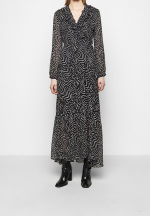 Žena nosící černé maxi šaty s bílým abstraktním tečkovaným vzorem, dlouhými rukávy, volánkovým výstřihem do V a černými kotníkovými vysokými botami.