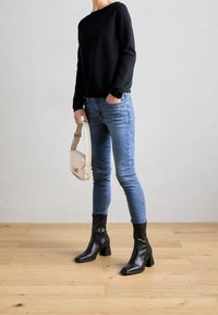 Czarny sweter z dzianiny, dopasowane jasnoniebieskie jeansy oraz czarne skórzane botki na obcasie sięgające kostki. Biała torebka na ramię o prostokątnym kształcie.