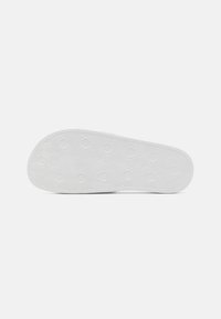 Hvid gummisål med en hexagonal mønster og tekstureret overflade for bedre greb, med afrundede kanter og flad profil.