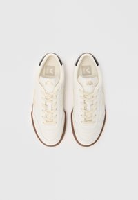 Sneakers brancos em pele com detalhes em castanho, atacadores planos, bico redondo e sola em borracha. Apresenta o logótipo da marca na lingueta e na lateral.