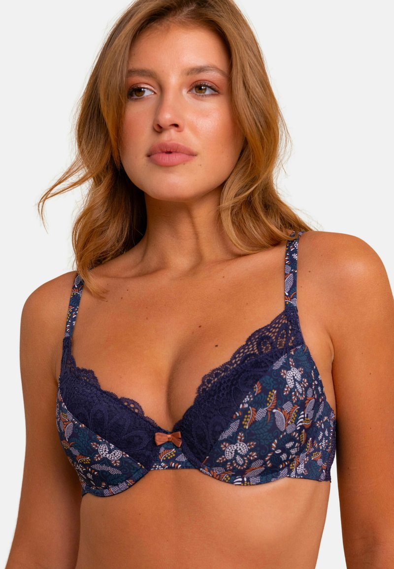 Soutien-gorge marine à motif floral, avec des bordures en dentelle et des bretelles réglables. Présente un petit nœud au centre. Tissu doux avec une finition texturée.