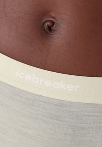 Fascia elastica di colore verde chiaro con logo "icebreaker"; superficie liscia; abbinata a un tono di pelle leggermente più scuro.