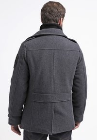 Ciemnoszary wełniany płaszcz z wysokim kołnierzem, usztywnianymi ramionami i karczkiem z tyłu. Posiada boczne kieszenie oraz naszywkę na lewym ramieniu.