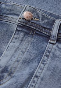 Tissu en denim bleu clair avec un gros plan sur un bouton en bronze, des coutures jaunes et une texture visible. Présente un design à cinq poches.