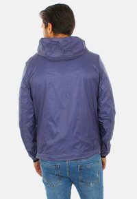 Giacca leggera navy con cappuccio, caratterizzata da una texture liscia e lucida e polsini elastici, abbinata a jeans in denim blu.
