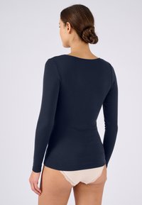 Langslavend marineblauw shirt van zachte stof; bevat een ronde halslijn en een getailleerd ontwerp, gecombineerd met lichtgekleurde ondergoed met kant.