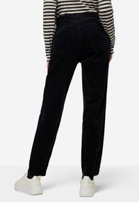 Zwarte corduroy broek met een recht model, voorzien van zakken, een hoge taille en een zachte textuur. Gecombineerd met witte sneakers.