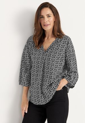 Schwarz-weiße gemusterte Bluse mit V-Ausschnitt, Dreiviertelärmeln und lockerer Passform. Die Textur ist glatt mit einem geometrischen Design.