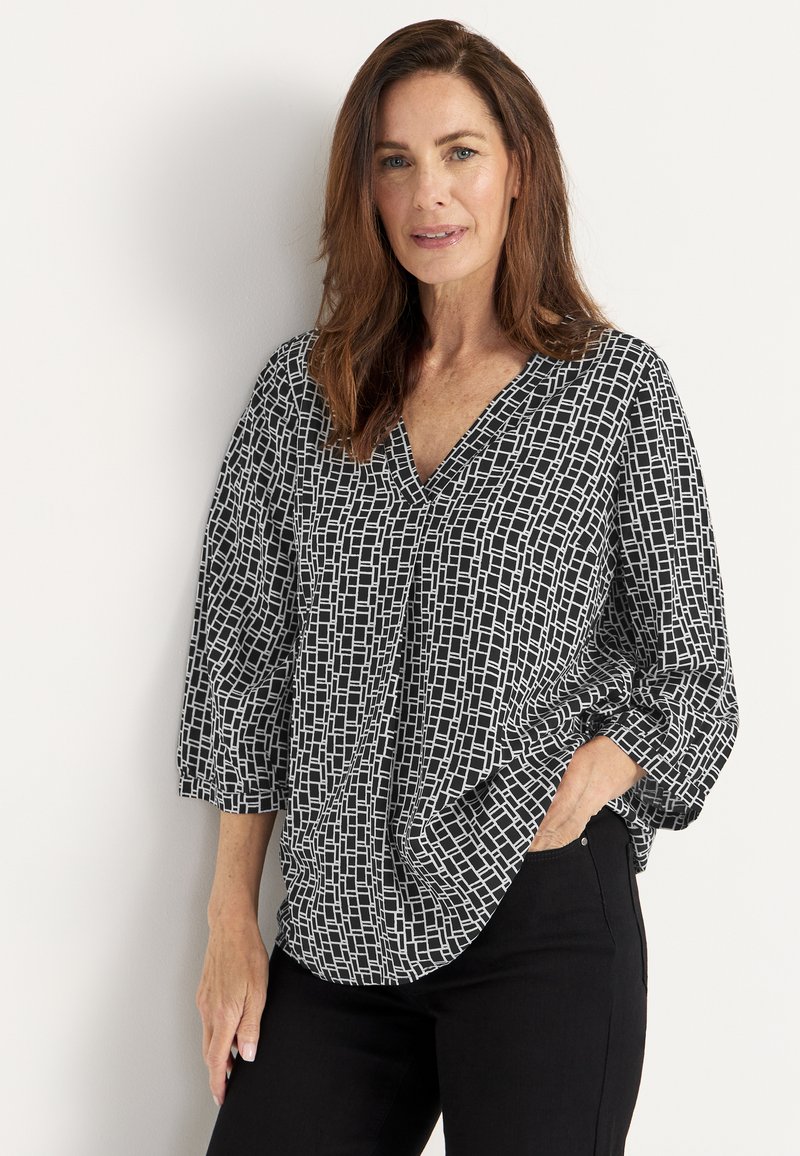 Schwarz-weiße gemusterte Bluse mit V-Ausschnitt, Dreiviertelärmeln und lockerer Passform. Die Textur ist glatt mit einem geometrischen Design.