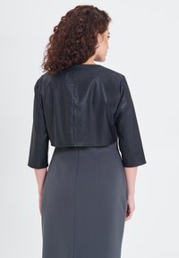 Giacca nera corta in pelle con maniche a tre quarti, abbinata a un vestito bodycon grigio caratterizzato da cuciture verticali.