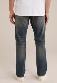 Siniset farkut suorelahkeiset, haalistunut pinta, kaksi takataskua ja hienovarainen kulumismalli, yhdistetty valkoisiin tennareihin.