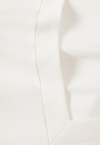 Tissu en coton blanc avec une texture lisse, comportant une couture et un bord structuré, créant un design épuré et simple.