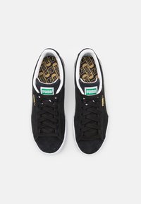 Czarne zamszowe sneakersy z białymi akcentami, z zielonym logo, czarnymi sznurowadłami i wzorzystą wkładką. Niski krój o zaokrąglonym kształcie.