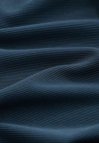 Tissu bleu foncé avec une fine texture côtelée horizontale et des plis doux créant de douces vagues sur la surface.