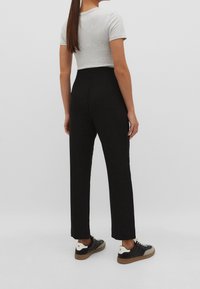 Šedé zkrácené tričko v kombinaci s černými kalhotami se zvýšeným pasem. Kalhoty mají rovný design a model nosí černé tenisky se světlejšími akcenty.