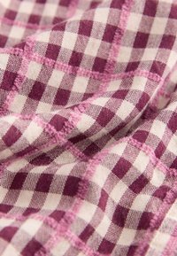 Woven fabric featuring a purple and white checkered pattern, with visible texture and stitching details. The design appears soft and flexible.