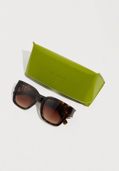 Γυαλιά ηλίου με μοτίβο χελώνας και φακούς καφέ διαβάθμισης δίπλα σε πράσινη ορθογώνια σκληρή θήκη με ανάγλυφο το όνομα της μάρκας, πάνω σε λευκή επιφάνεια.