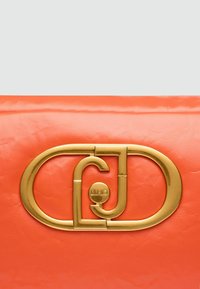 Geantă de mână din piele coral cu o textură netedă, evidențiind un sistem de închidere proeminent din metal auriu, cu litere intercalate și un accent circular cu logo.