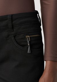 Zwarte denim jeans hebben een klein, ritsvak met een leren trekband. De stof heeft een gladde textuur en een aansluitend ontwerp.