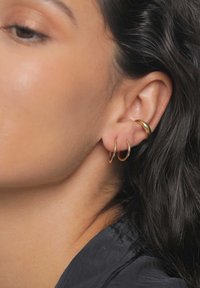 Golden hoop earrings in various sizes, three small hoops stacked, one larger hoop above, displayed against a smooth skin texture.