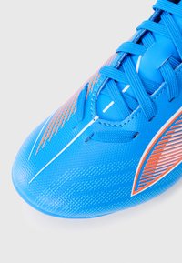 Zapatilla deportiva azul con un upper texturizado, acentos naranjas contrastantes y cordones blancos. Presenta una forma aerodinámica y un cuello acolchado.