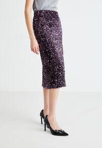 Violetti paljeteilla koristeltu kynähame, jossa on tiukka siluetti, polvipituus, kiiltävä pinta ja sivuvesiketju, yhdistettynä mustiin korkokenkiin.